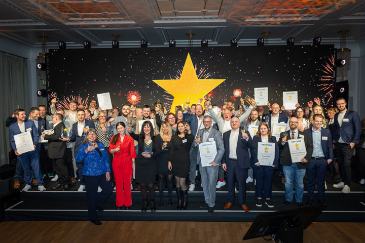 Gruppenfoto einer großen Gruppe ausgezeichneter Personen bei einer Preisverleihung auf einer Bühne. Im Hintergrund sind ein großer gelber Stern, Feuerwerk und mehrere Scheinwerfer zu sehen; einige Teilnehmende halten Urkunden und Trophäen in die Kamera.